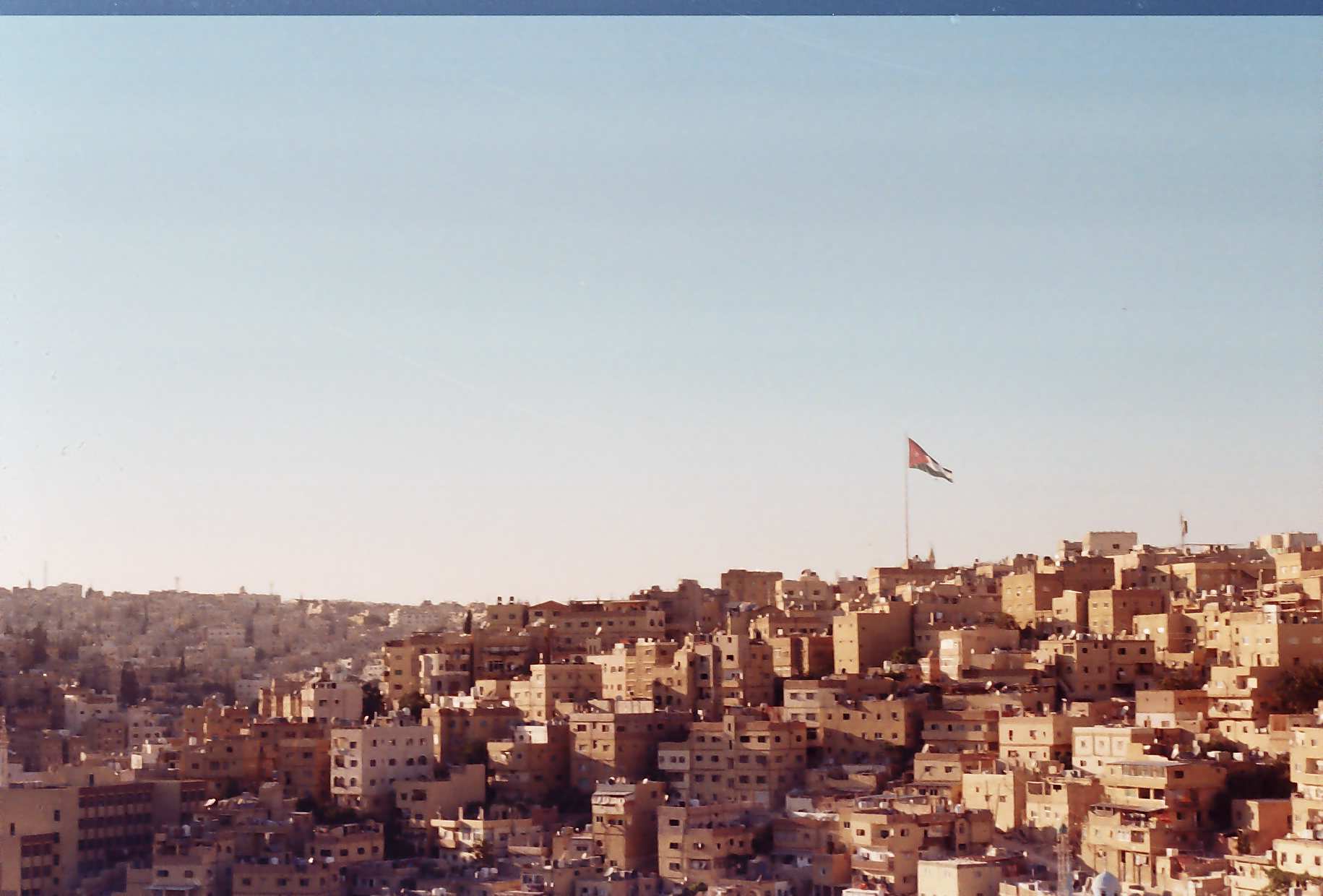 Cityscape of Amman with buildings and the flag of The Hashemite Kingdom of Jordan on a clear day